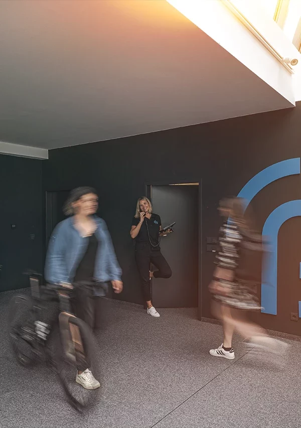 Mehrere Personen gehen durch ein Büro mit dem paricon-Logo an der Wand. Eine Frau steht telefonierend in der Nähe des Logos.