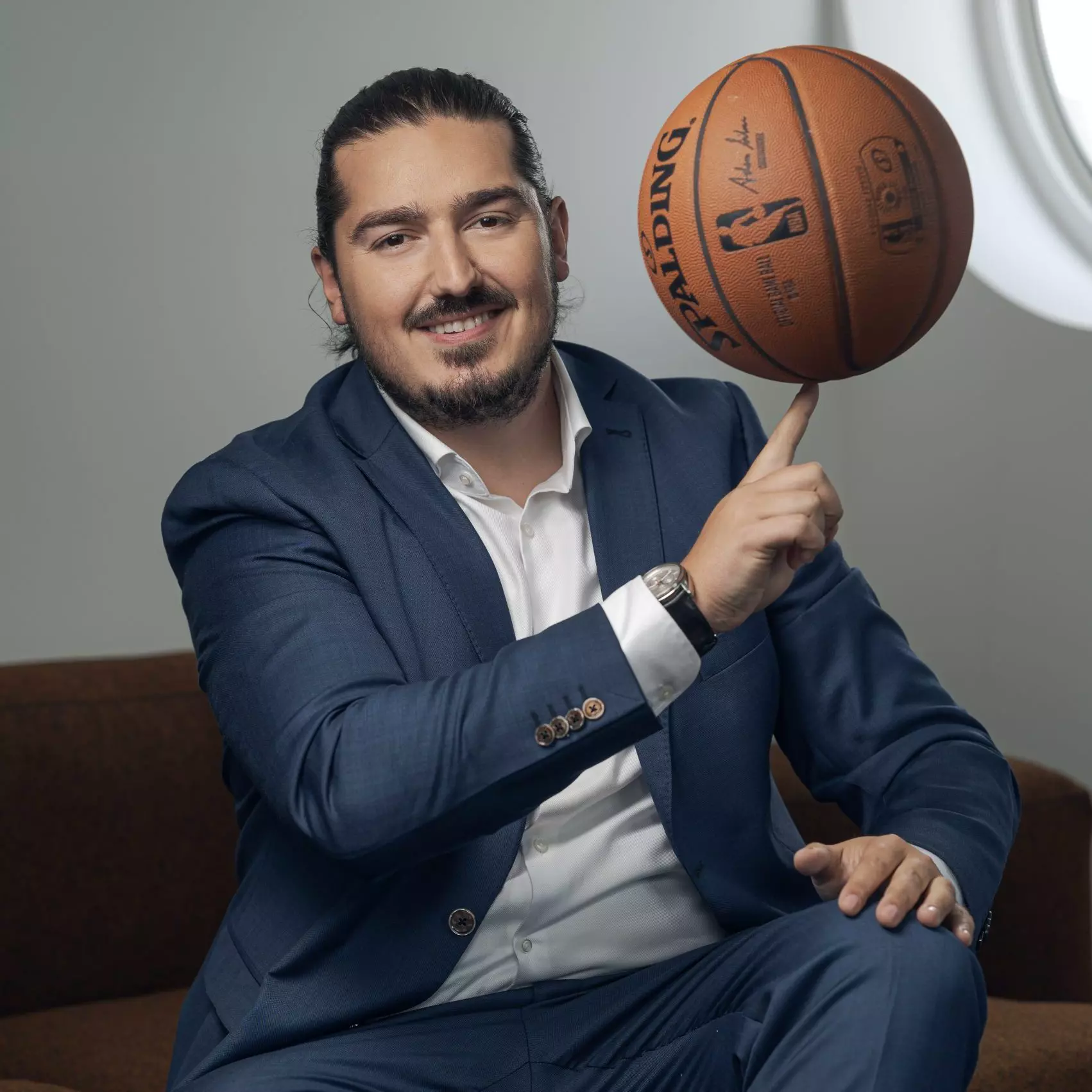 Kujtim Ljaci in einem Anzug, er dreht einen Basketball auf seinem Finger und lächelt.