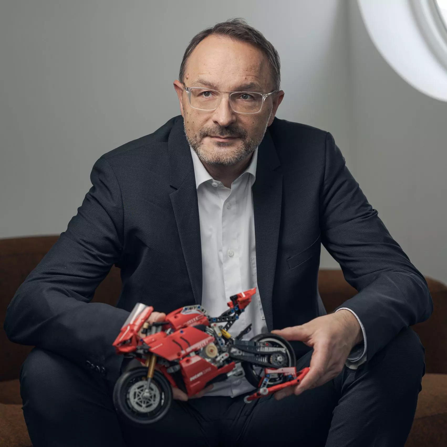 Michael Müller Jacquet in einem dunklen Anzug, er hält ein Modell eines roten Motorrads in den Händen.
